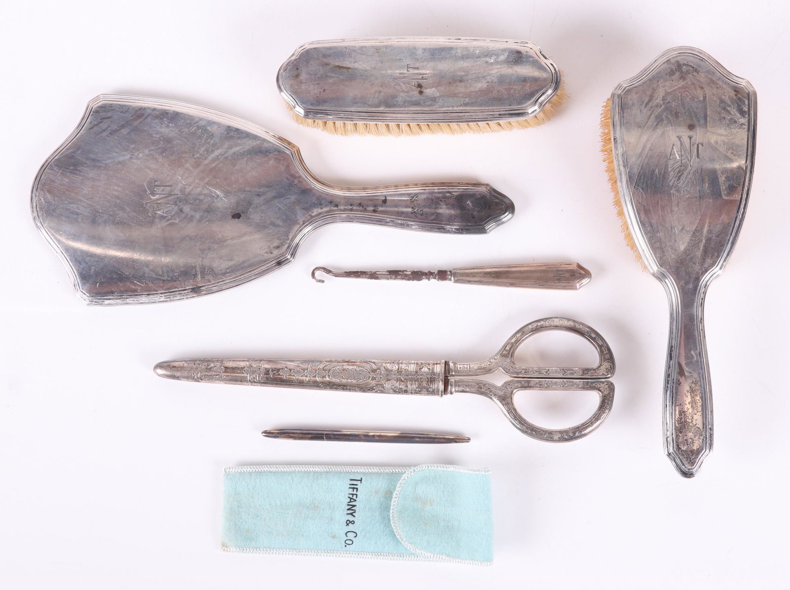 Group of Sterling Silver Items by Tiffany: Comprising: a dresser set with 9" brush, 6" clothes brush, 10 3/4" hand mirror, and 6" button hook, all monogrammed; 9 1/2" scissors with sheath, both with engraved foliate and scrolling geometric dec