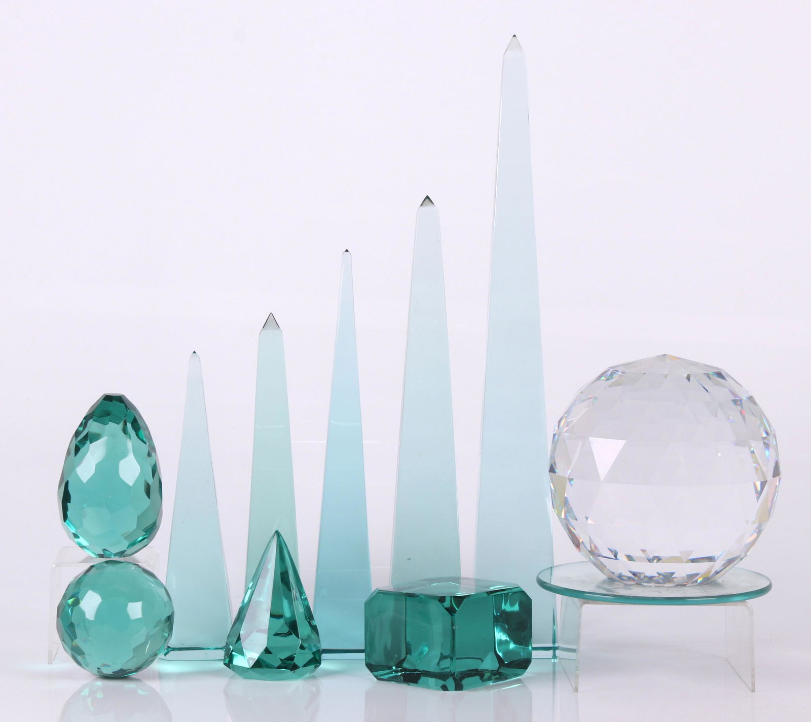 Ten Glass Paperweights and Obelisks: Comprising: five graduated blue/green obelisks; three green faceted examples, one egg form, one spherical, the other conical; a green cube form example; a large faceted clear glass spherical piece mou