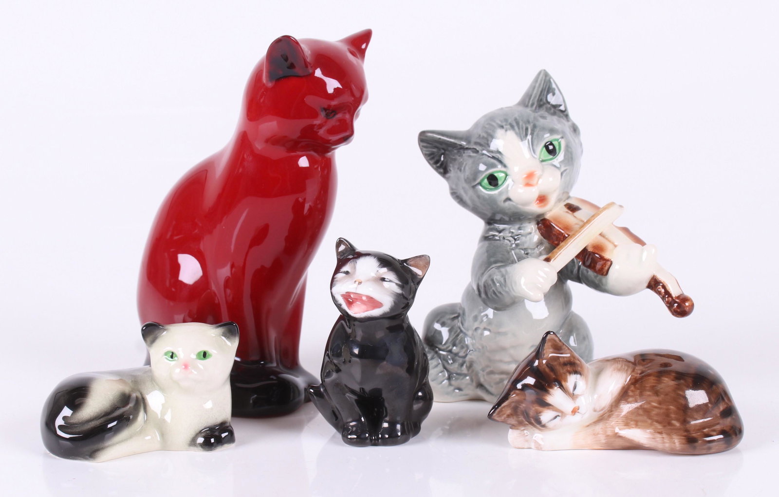Five Porcelain Cats, Royal Doulton and Goebel: Comprising: a Royal Doulton Flambe cat, Royal Doulton "Lucky", a sleeping cat also by Royal Doulton, and two Goebel examples. Dimensions: From 2" x 2 1/2" to 4 1/2" x 3", the heights range from 1 1/2"