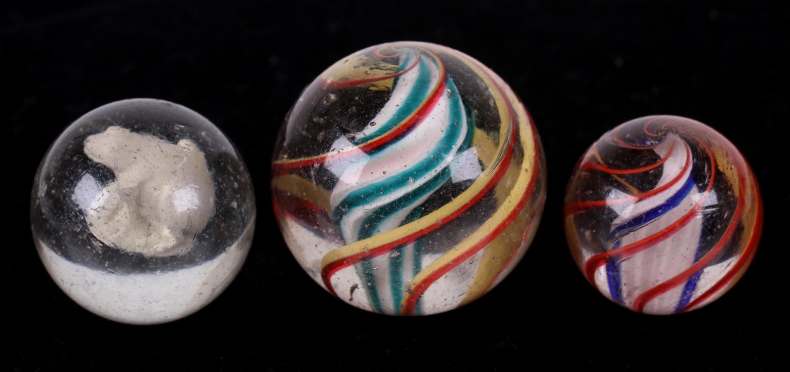 Three Antique Toy Glass Marbles: Two swirl examples and a frog sulphide. Dimensions: From 1 1/2" to 2" in diameter. Provenance: From a local collection.