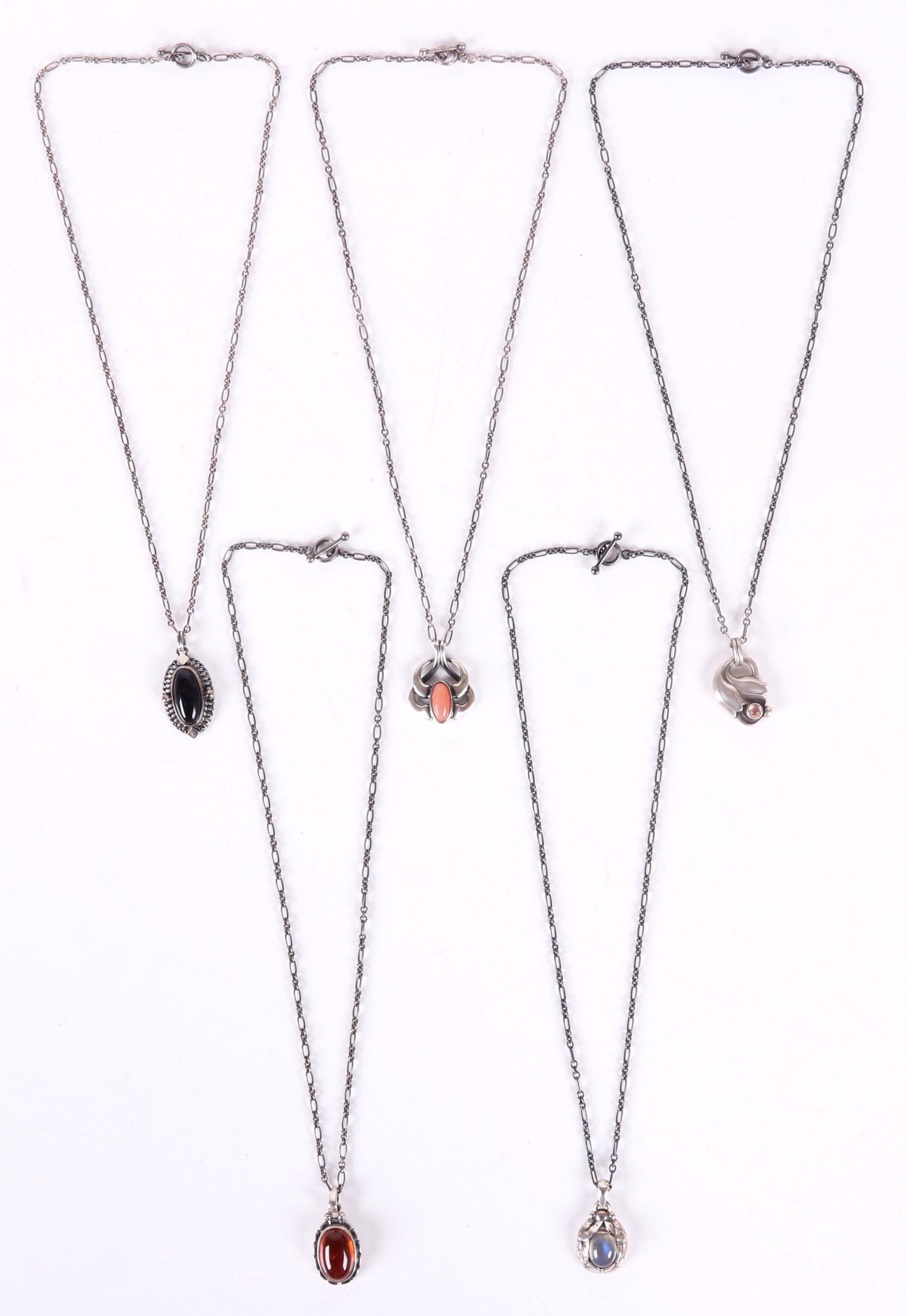 Five Georg Jensen Sterling Pendants: An amber example dated for 2001, a 2004 example with black onyx, a 1999 example set with rose quartz, a 1997 pendant set with labradorite, and 2006 example set with coral. All retain the original cust
