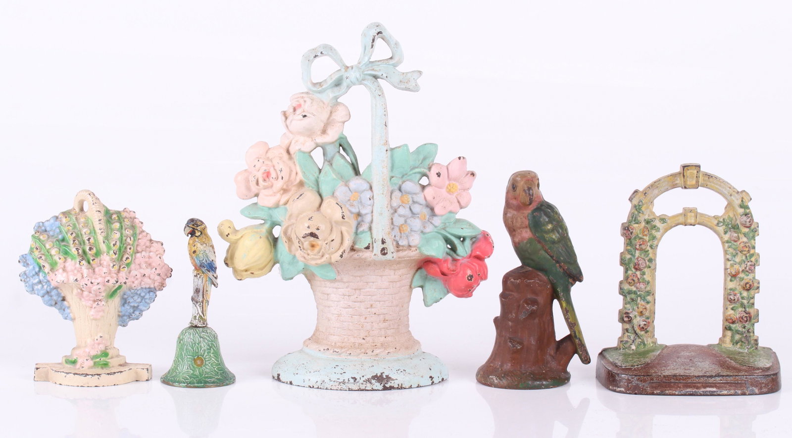 A Group of Cast Iron and Brass, Doorstops, Etc...: All from the first half of the 20th century, comprising: a brass polychrome painted bell with parrot terminal, a cast iron parrot figure perched upon a stump and three floral decorated cast iron doors