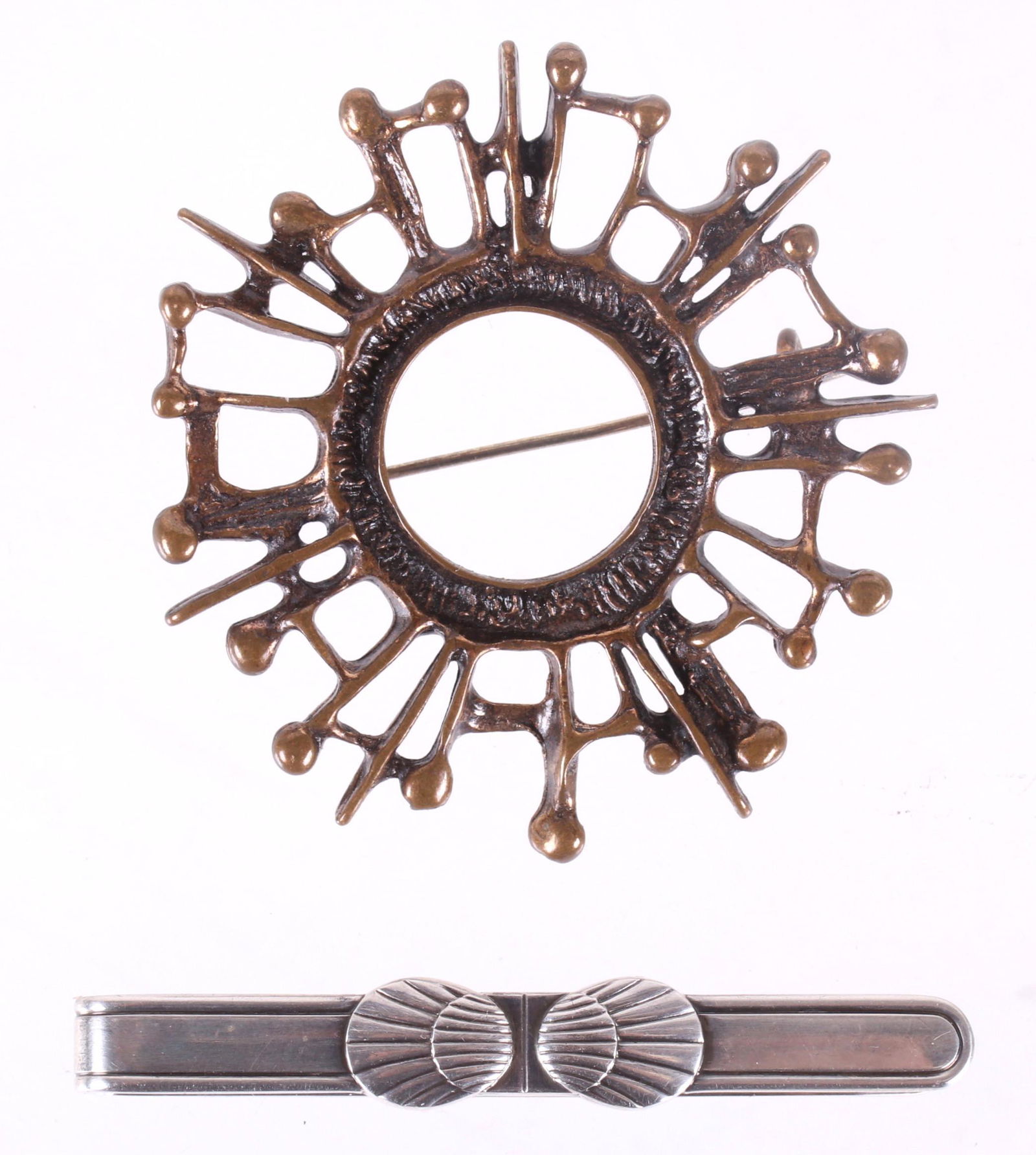 Two Pieces, David Andersen and Georg Jensen: A modernist pin in bronze by David Andersen and a sterling silver shell decorated tie clip by Georg Jensen. Dimensions:The pin is 2" and the tie clip measures 2 1/8" x 1/4" and weighs 0.36 troy ounces