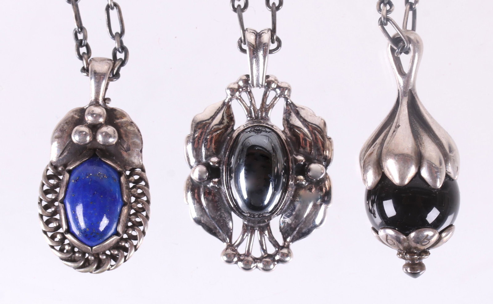 Three Georg Jensen Sterling Pendants: A 1992 pendant of the year set dated and set with lapis lazuli, a 1991 example set with onyx, and the 2000 pendant which is dated and set with Hematite. Dimensions:From 1 1/8" to 1 1/4" long. The tota