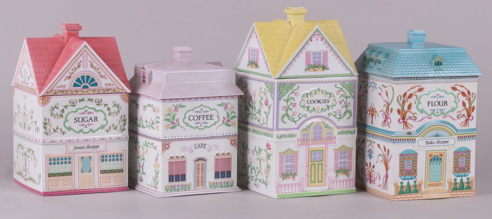 Four Lenox Village Porcelain Jars: Each in the form of a house, labeled for cookies, coffee, flour and sugar. Dimensions: From 5 1/4" x 5 1/4" to 5 1/2" x 5 1/2", the heights range from 9" to 10 1/2".