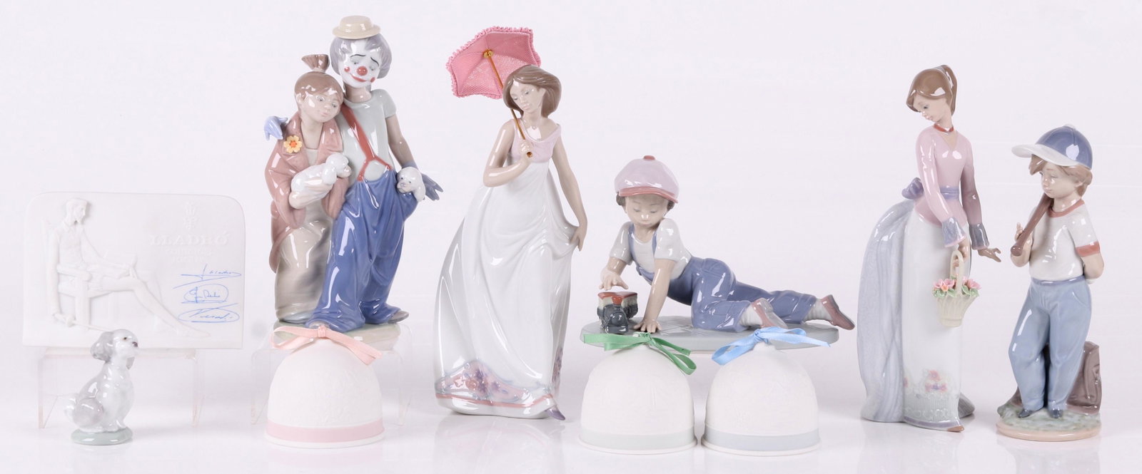 Six Lladro Porcelain Figures: "Pals forever", "Afternoon Promenade", "All Aboard", "Can I play?", "Basket of love", three bells, a figure of a dog, and a Lladro plaque. Dimensions: The boxes range from 11" x 6" x 5" to 12" x 7 1/2