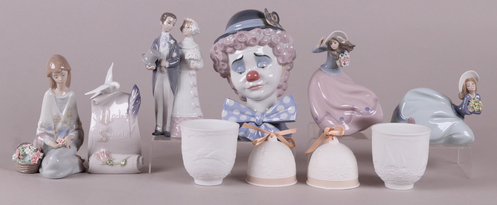 A Group of Lladro Figures, Etc...: A Lladro Society plaque, "Spring Bell", "Damita aganchada", "Dolphins at play" cup, "Sad Clown", "Wedding", "The Seas" cup, "Fall bell", "Cancion de Primavera", and "Damita arrodillada". All retain th
