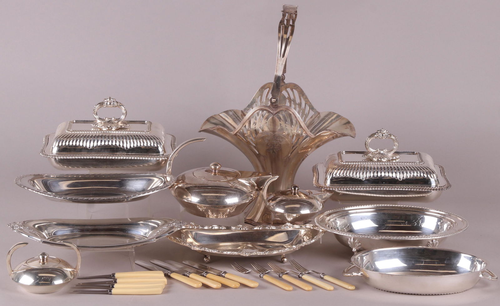 A Large Group of Silver Plated Tableware: Comprising: an unmarked three piece modernist tea set, three oval serving trays, a pair of Sheffield covered servers, a single covered server with hoof feet, a Derby basket form vase, and a group of f