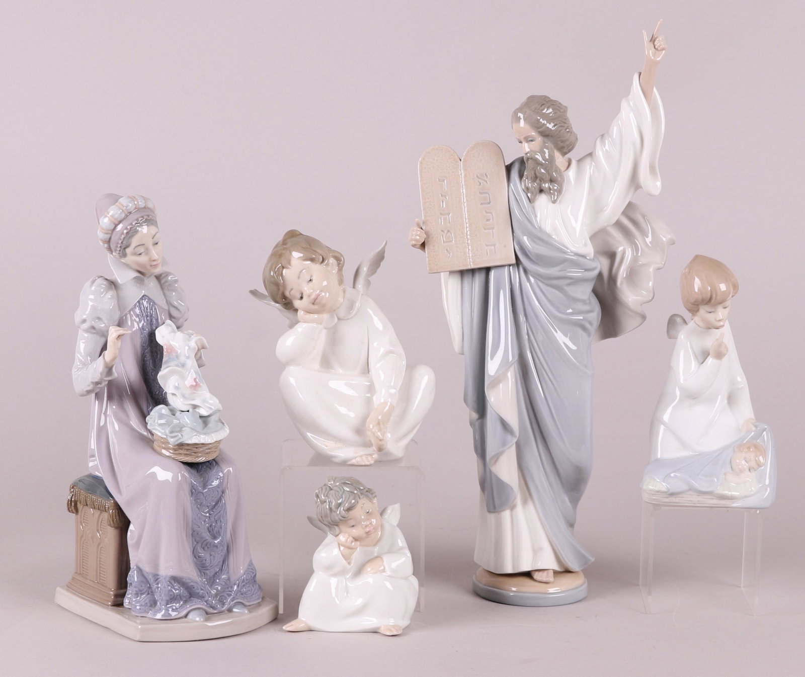 Group of Lladro Porcelain Figures: Comprising: "Sewing a Trousseau", "Angel with Baby", two sizes of "Angel Thinking", and "Moses" which retains the original box. Dimensions: From 3 1/2" x 3" to 6" x 4 1/2", the heights range from 4 1/