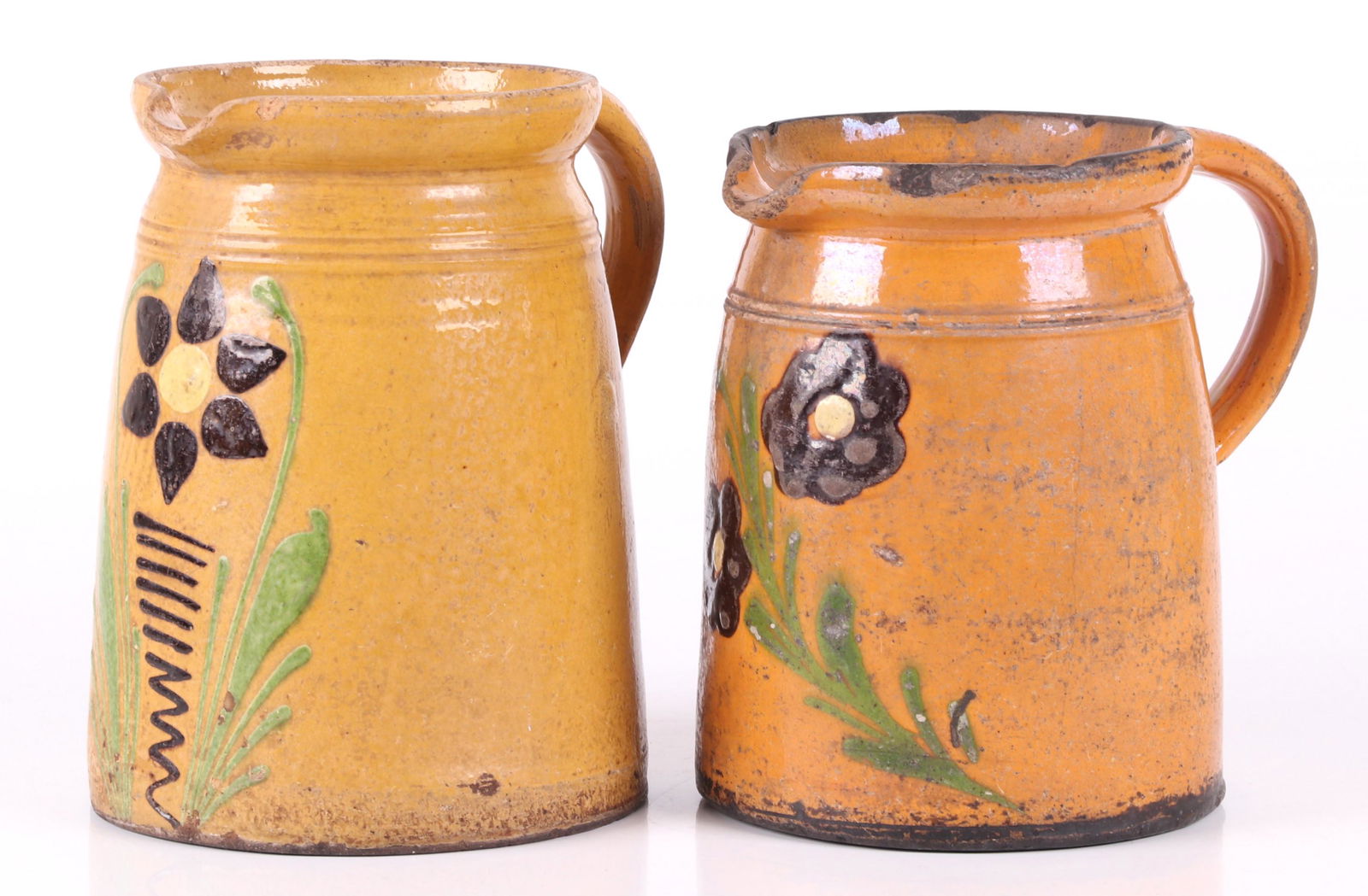 Two French Redware Pitchers: Each with a yellow glaze and floral decoration. Dimensions: The smaller is 8 1/2" x 6" and 8 1/2" tall and the larger is 8 1/2" x 6" and 9 1/2" tall. Provenance: From a local collection.