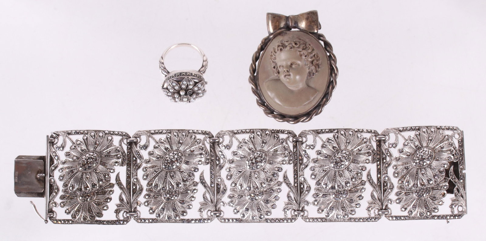Sterling Jewelry, Poison Ring, Etc...: A sterling and marcasite bracelet with floral decoration, a sterling marcasite and seed pearl poison ring, and a silver brooch (unmarked) set with a ceramic head of a putto, signed "handmade by Moni, 