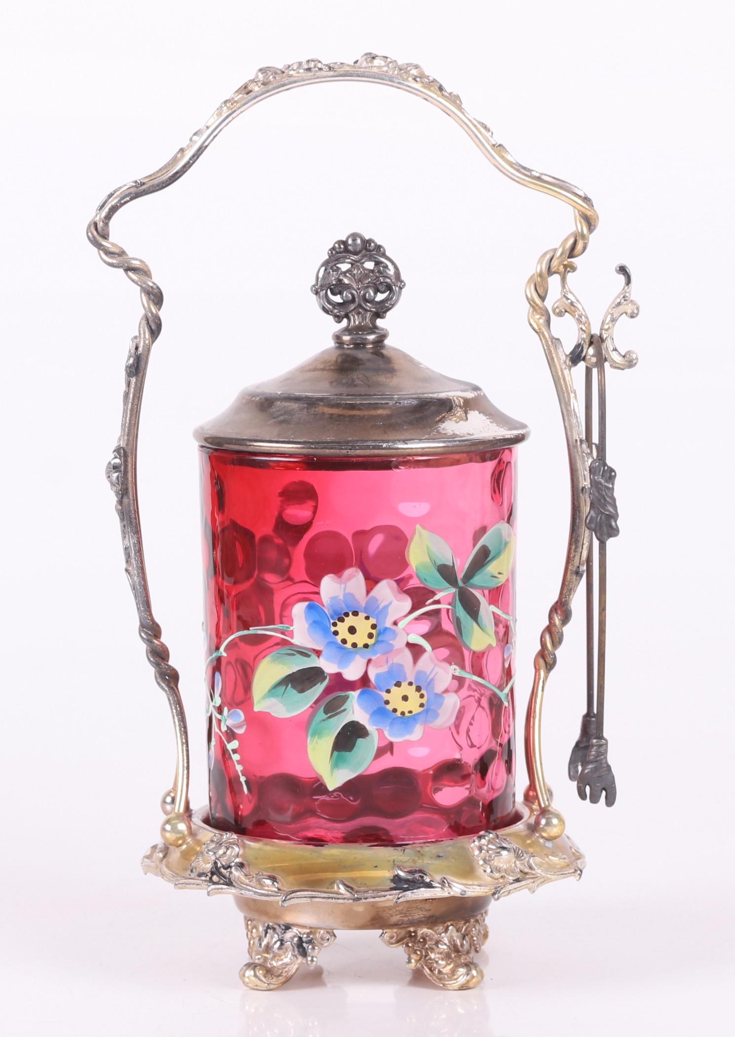 A Cranberry Glass Pickle Castor: Late 19th century, by Forbes, with a thumbprint pattern and enamel decorated cranberry glass jar and floral decorated stand. Dimensions:5" in diameter, the overall height is 9 1/2". Provenance:From a 