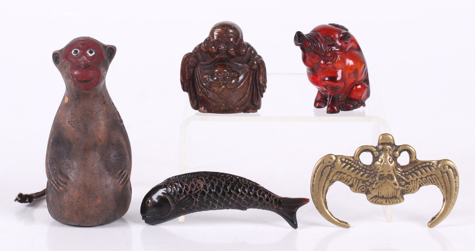 A Group of Japanese Netsuke, One Umimatsu: Comprising: an umimatsu netsuke of a carp, an example carved as a pig which appears to be amber, an example depicting Hotei with a child, a large ceramic netsuke in the form of a monkey with a rattle 