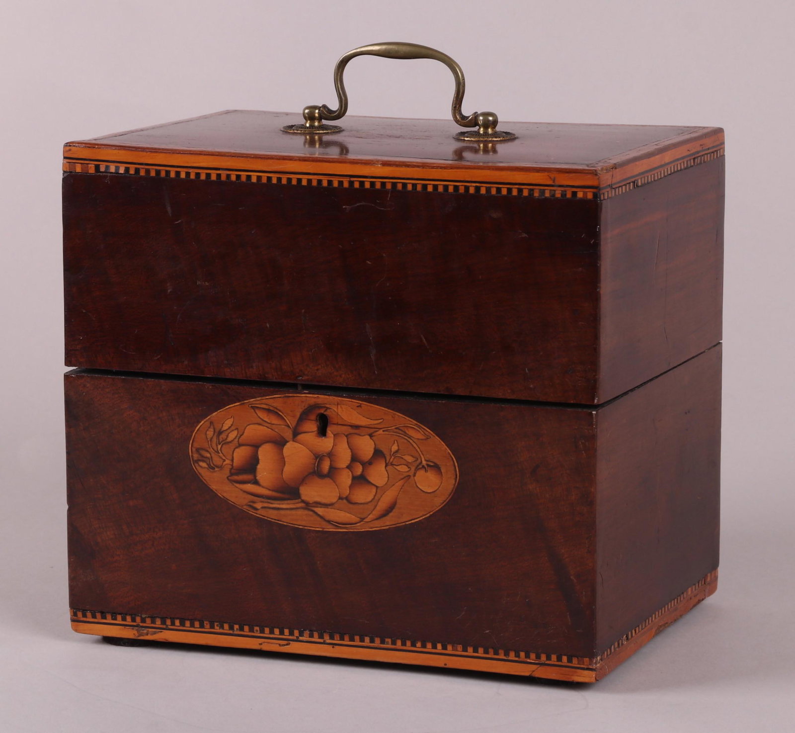 A George III Cased Decanter Set: Circa 1800, the mahogany case with dentil banding, bail handle and inlaid paterae. The hinged lid opens to reveal two small wine glasses with gilt piping and a set of six glass bottles with gilt decor