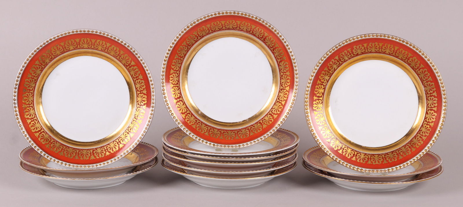 A Set of KPM Porcelain Dinner Plates: 19th century, each with an orange and gilt border that features palmettes and beading. 12 plates. Dimensions: Each is 9 1/2" in diameter. Provenance: From a Main Line Estate