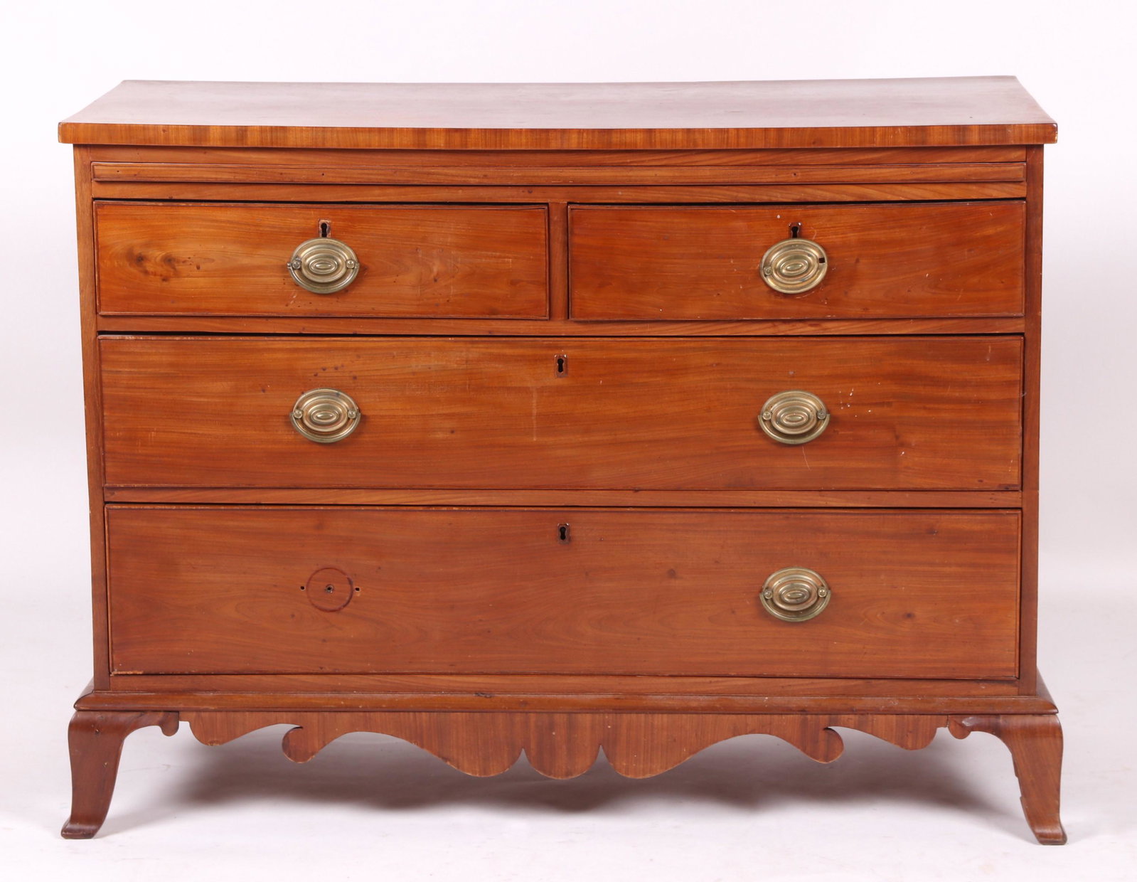 An Unusual Mahogany Hepplewhite Chest of Drawers: Early 19th century. With French feet, deeply scalloped apron, a configuration of four dovetailed and cockbeaded drawers below a pull out writing surface and the conforming rectangular top. Dimensions: