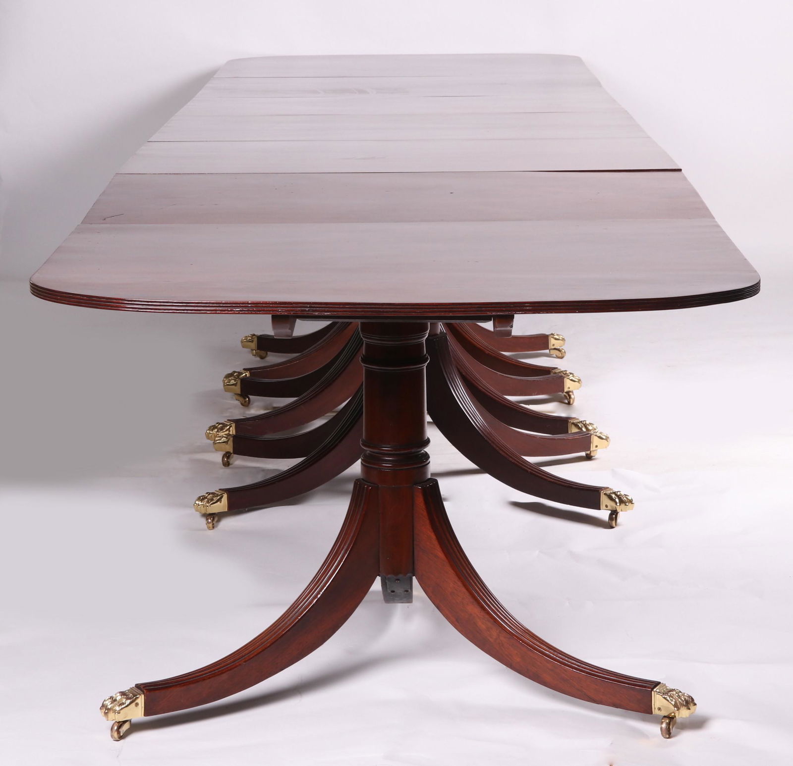 A Duncan Phyfe Style Mahogany Dining Table: 19th century. A five pedestal example that opens to 19 feet. Each tripod support with reeded saber legs that end in paw form brass casters. The edges of the top are reeded. Table consists of three cen