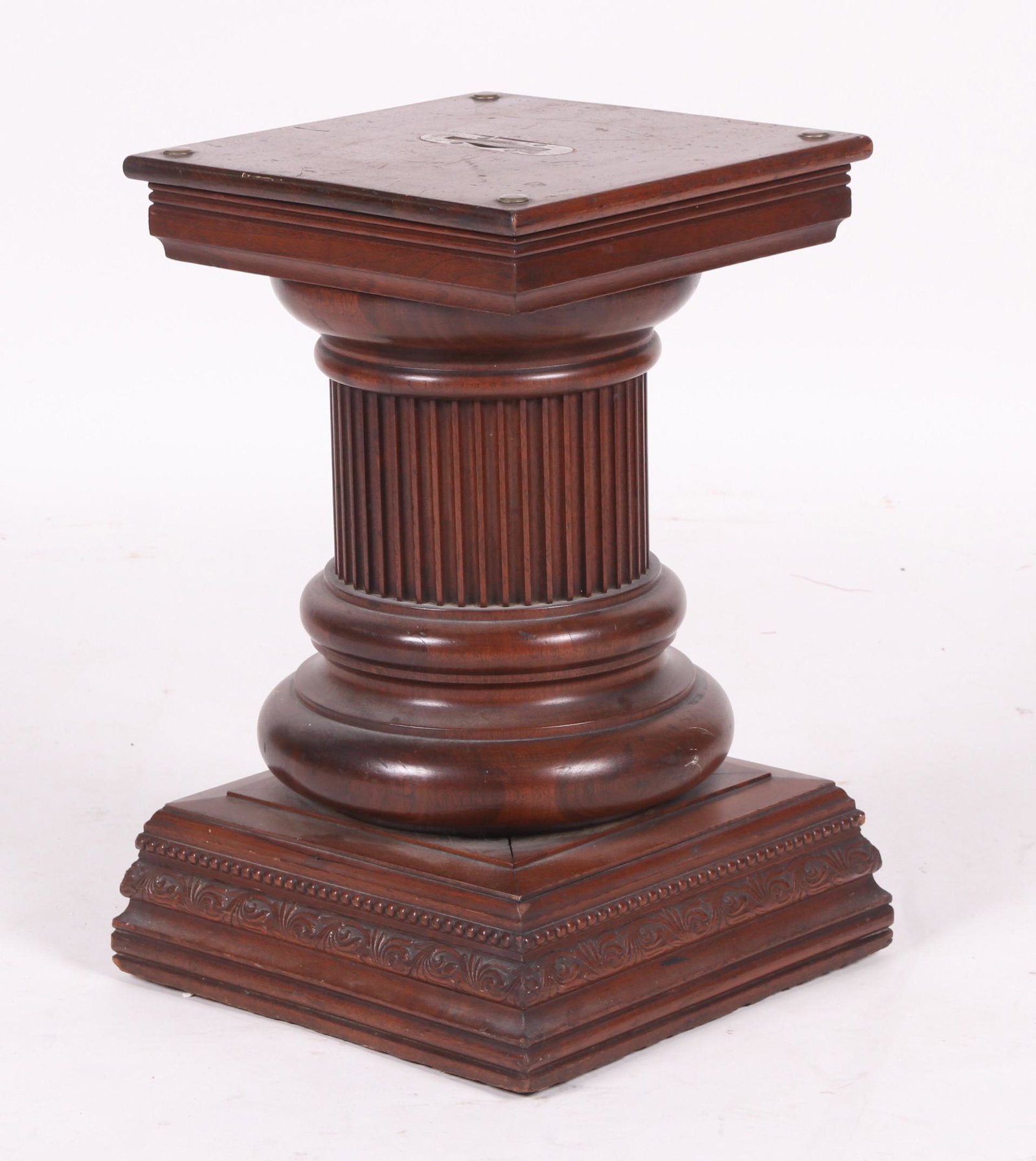 A Walnut Casket Podium, c. 1900: With a square molded base that features foliate carving and beading below a fluted column. All below the square molded top that features a central collapsible handle. Dimensions: 14" x 14", 21" tall. 