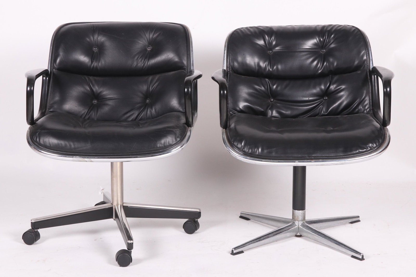 Two Charles Pollock for Knoll Armchairs: Two swivel office chairs with cross form chrome bases. A seat with loop arms, chrome trim and black vinyl upholstery. The bases are slightly different. One features casters. Dimensions: Each is 26" ar