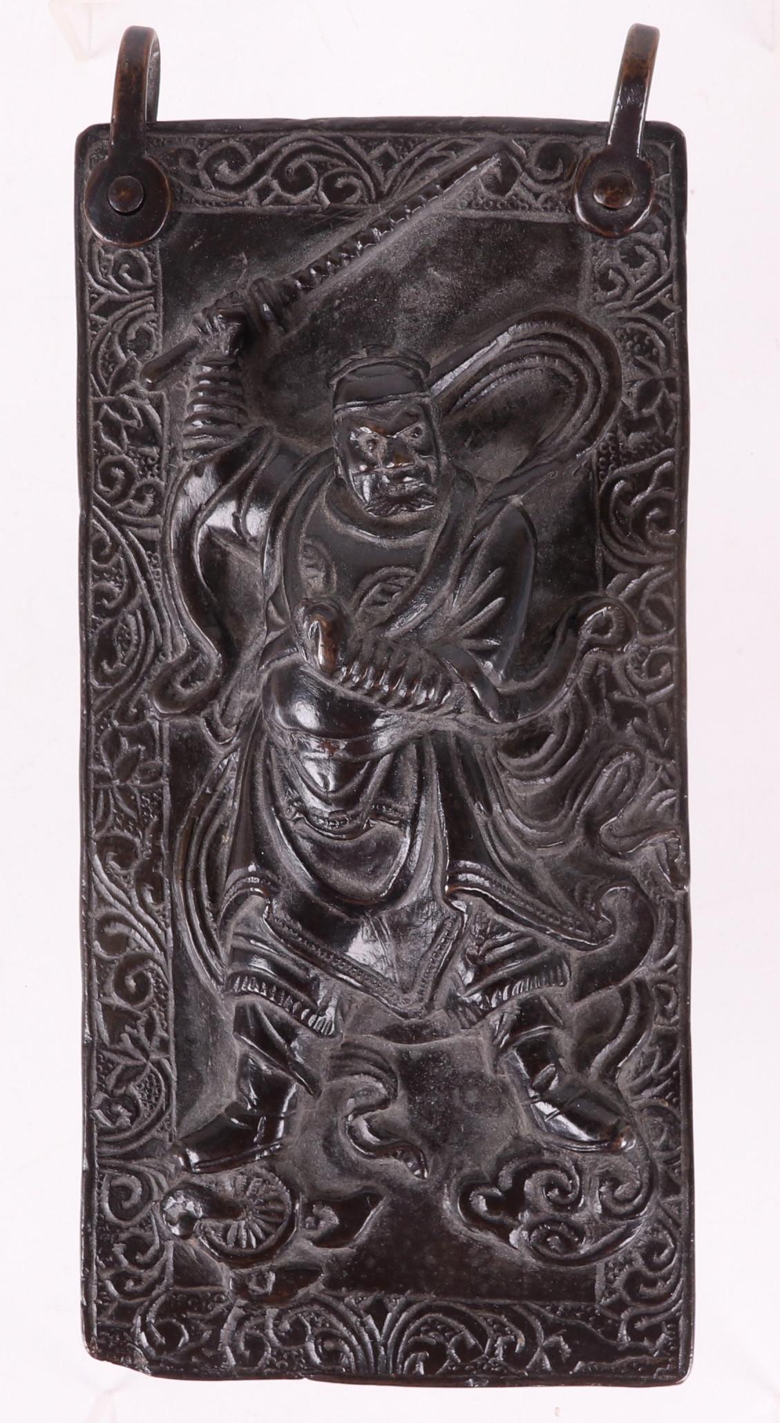 A Chinese Bronze Plaque, Warrior: A Qing Dynasty bronze plaque with hanging rings, high relief central warrior and text in Chinese Characters verso. Dimensions: 8" x 4" x 1 3/4". Provenance: From a Pittsburgh estate.
