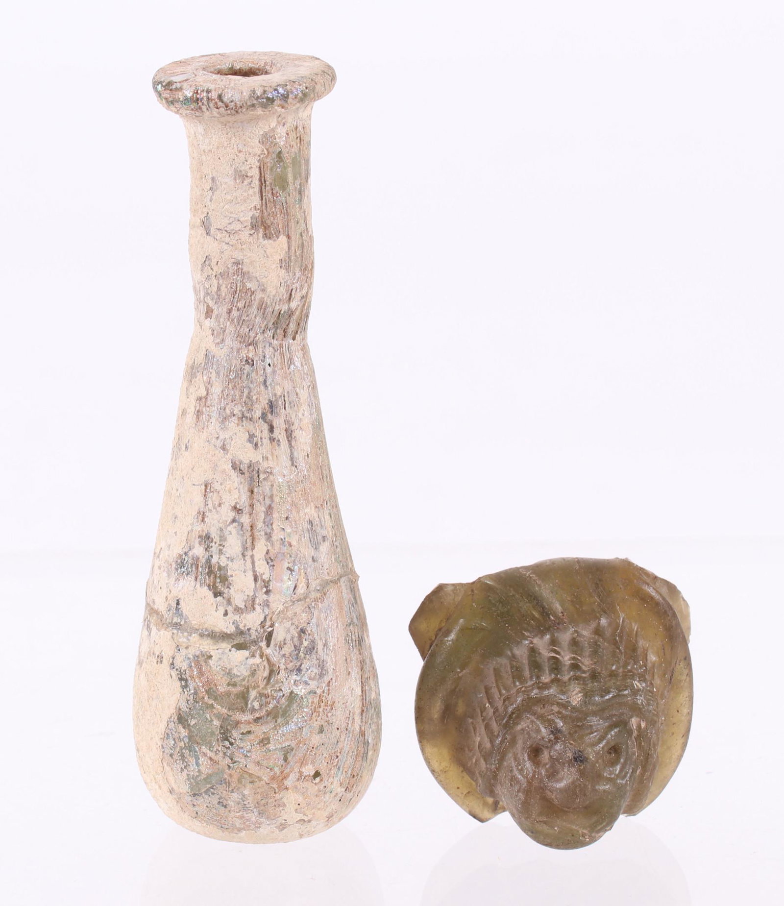Two Pieces of Ancient Roman Glass: An unguent bottle of typical form and a fragment with mask decoration. Dimensions: The fragment is 1 1/4" x 1 1/4" x 3/4". Provenance: From a PA estate.