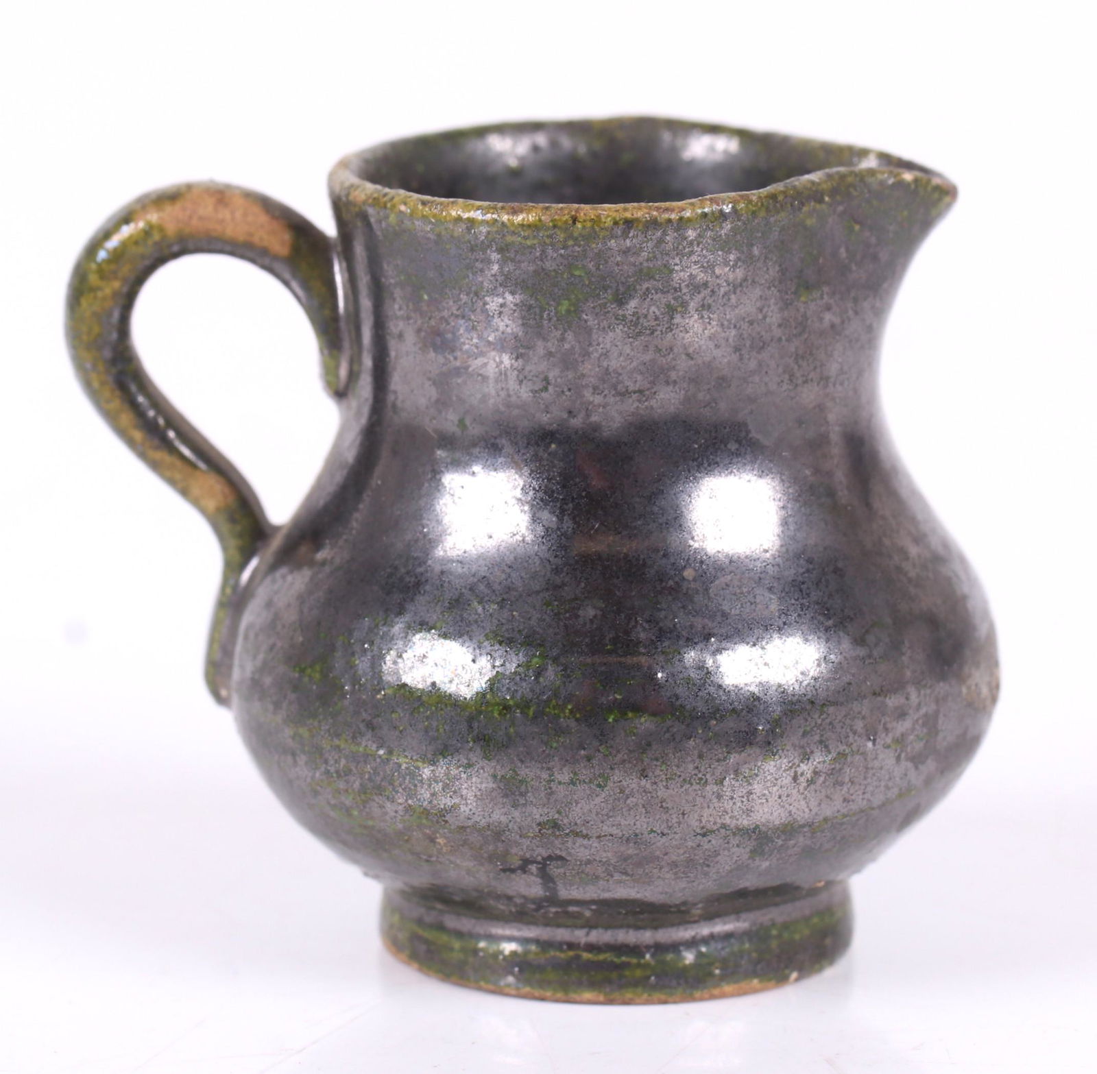 A Miniature Redware Pitcher, 19th Century: With a circular foot, ear form handle and a green glaze. Dimensions: 1 3/4" in diameter, 1 7/8" tall. Provenance: From a PA estate.