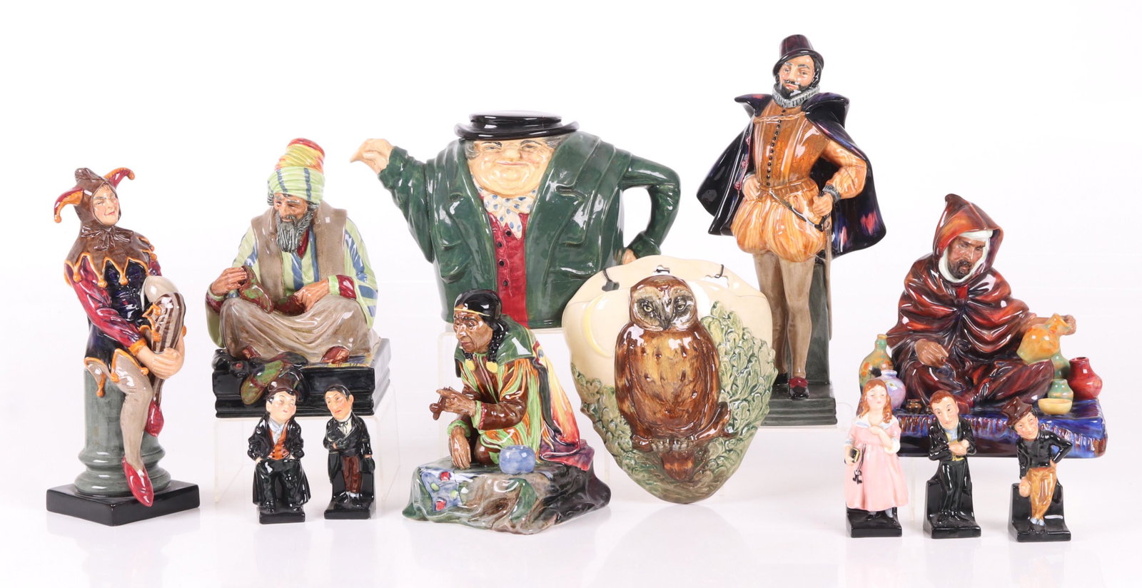 Large Group of Royal Doulton Pottery: All 20th century, comprising: The Jester, an owl decorated wall pocket, Sir Walter Raleigh, The Potter, Calumet, Cobbler, a Tony Weller teapot, and five small Dickens characters. Dimensions: From 1 1/