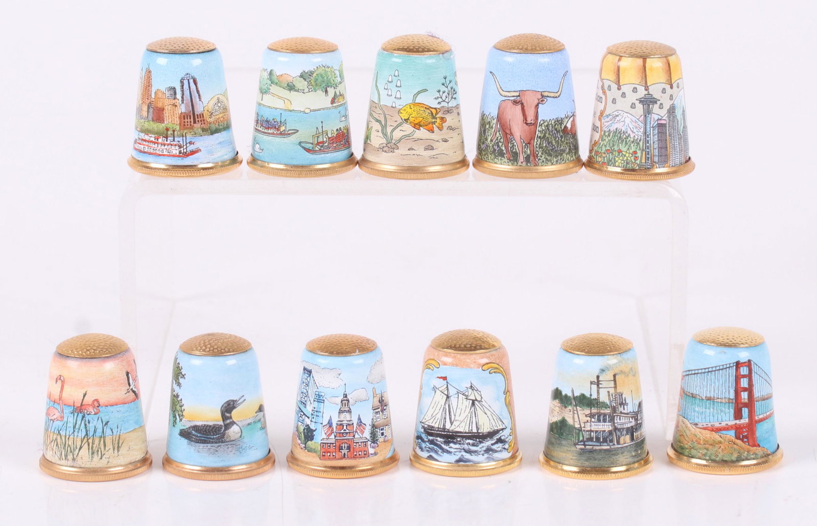 A Group of Halcyon Days Enamel Thimbles: Eleven examples, all commemorating a TCI convention. Dimensions: Each is about 1" tall. Provenance: From a local estate.
