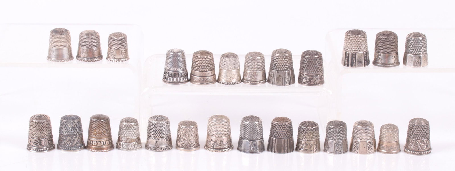 Twenty Five Sterling Silver Decorated Thimbles: Various sizes and decoration, makers include Simons Brothers, Waite, Thresher Co., and Ketcham and McDougall. Dimensions: From size 7 to 10, the total approximate weight is 3.58 troy ounces. Provenanc