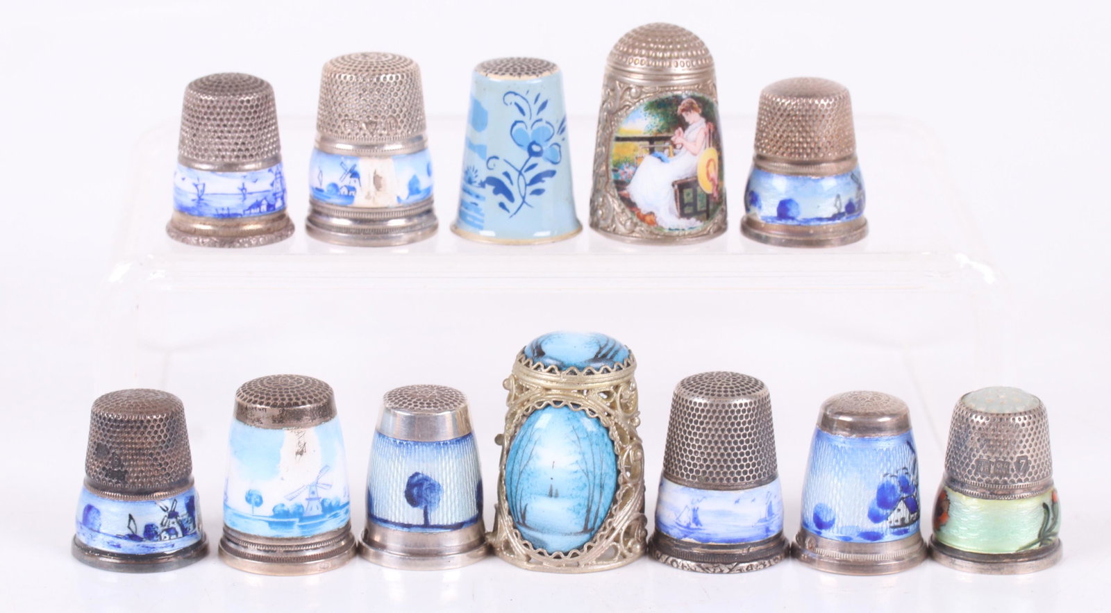 A Group of Enameled Sterling Thimbles: Twelve examples, most with blue and white landscape decoration, two floral examples and a good thimble decorated with a woman sewing titled, "The Seamstress". Dimensions: Various sizes, the total gros