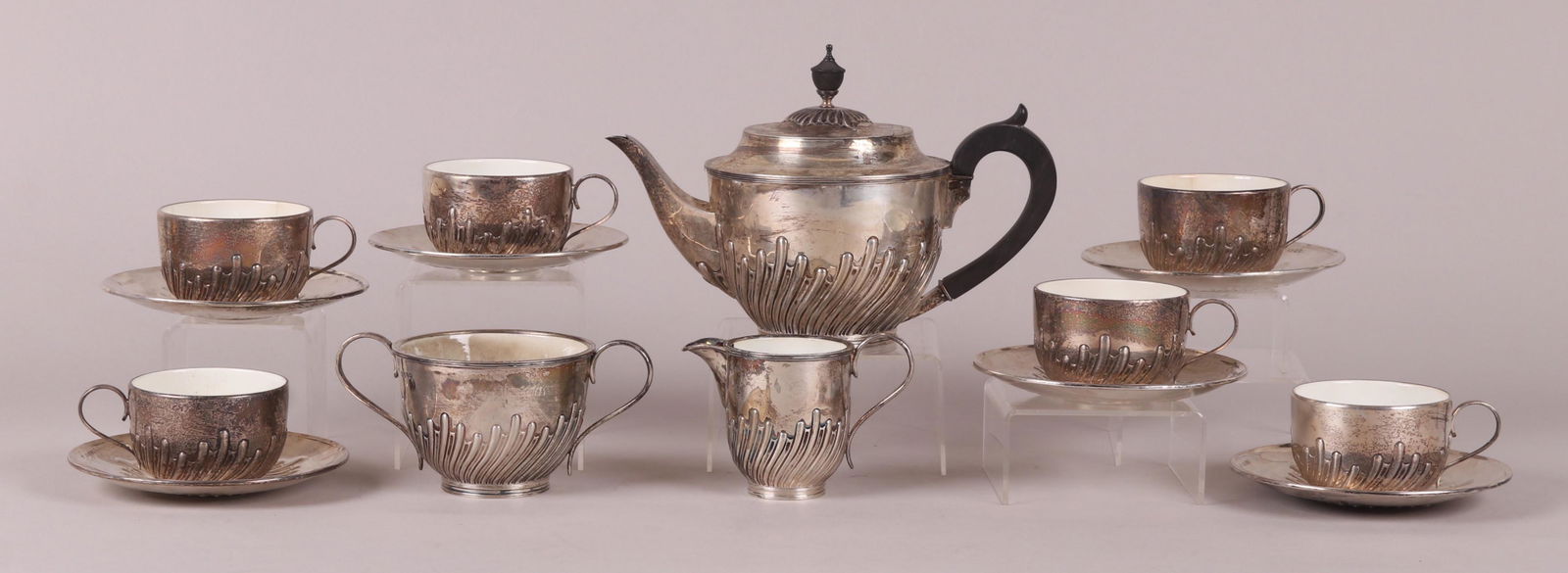An English Sterling Tea Set: Hallmarked for London, 1889 and the maker William Hutton & Sons. There is a teapot, sugar, creamer and six cups with saucers. All pieces except for the saucers are porcelain lined. Dimensions: From 4"