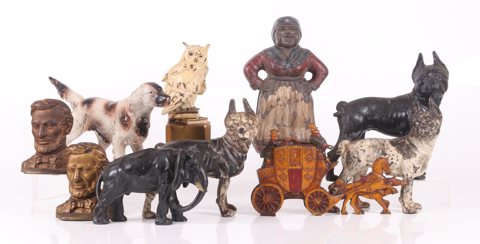 A Group of Cast Metal Items, Doorstops, Etc...: Comprising: four dog form cast iron doorstops, a pair of Lincoln bookends, an English coach cast iron doorstop, a white metal owl standing upon books, a cast white metal elephant and a cast iron Aunt