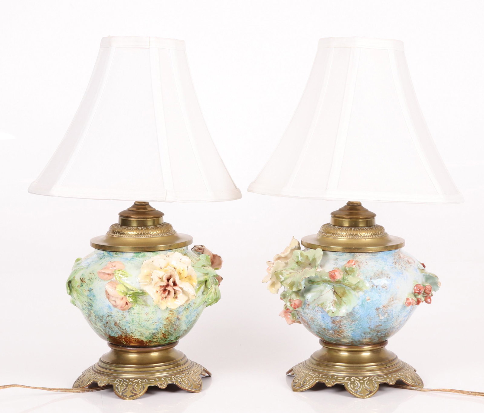 A Pair of French Barbotine Majolica Lamps: Late 19th century, each with typical high relief floral decoration. Bronze mounted. Two shade harps are included in the lot. Dimensions: Each is 9" in diameter and 18 1/2" tall including the shade.