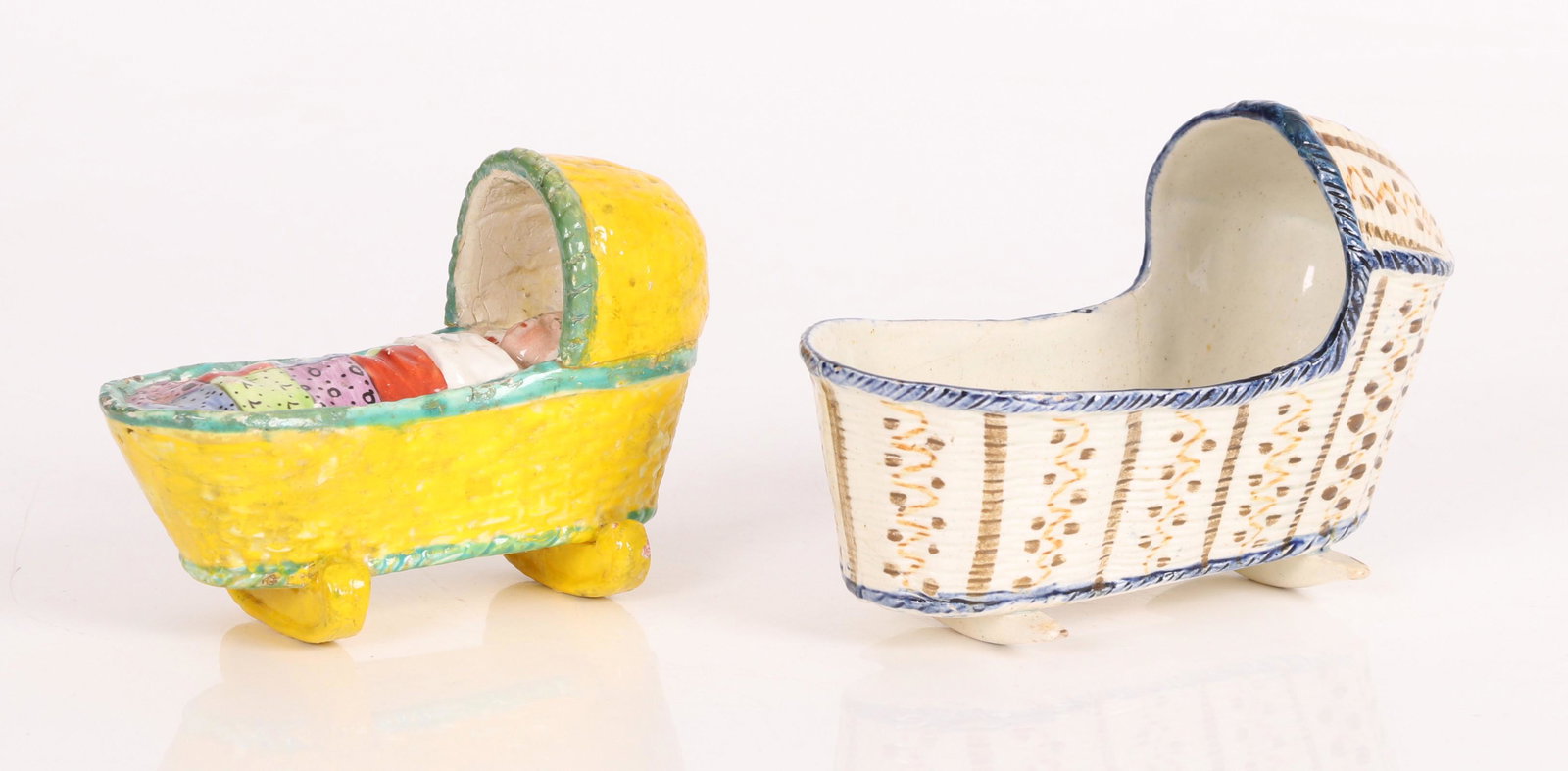 Two English Staffordshire Pearlware Cradles: Early 19th century, one in canary yellow glaze having in the form of a child sleeping in a cradle and the other of open form. Dimensions: The larger measures 5" L x 3.5" H x 2.5" W. The smaller measur