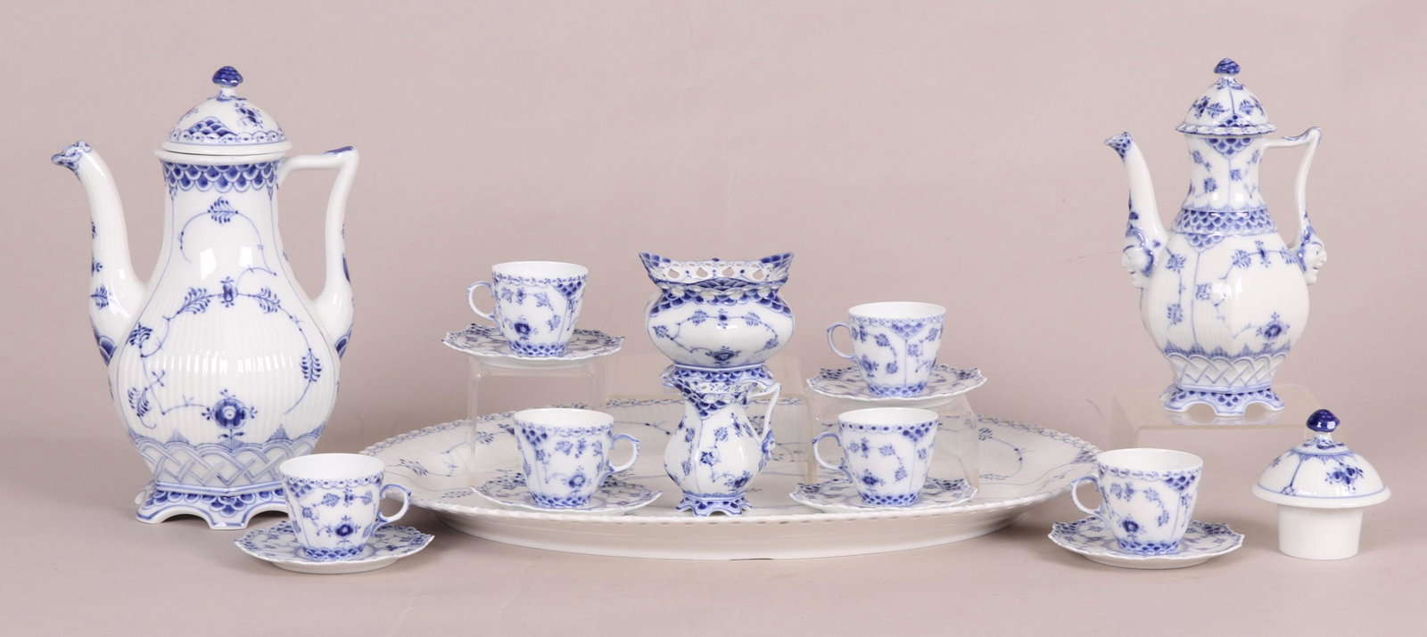 Seventeen Pieces of Royal Copenhagen Full Lace: To include a platter, coffee pot, teapot, cream & sugar, six demitasse cup & saucer sets, and a spare lid. Dimensions: The platter measures approximately 18" W. The larger coffee pot measures 10.5" H 