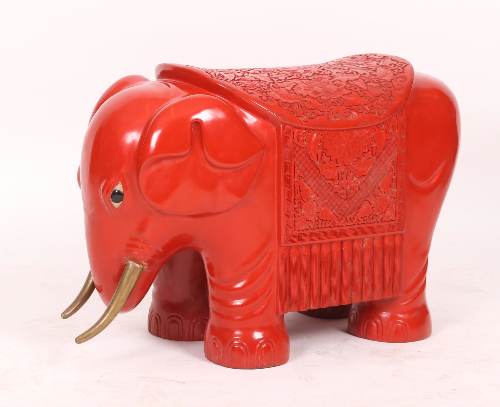 A Chinese Cinnabar Elephant Form Stool: 20th century, with brass tusks and eyes made of glass and mother of pearl. Dimensions: 32" x 13", the height is 19". Provenance: From a Main Line estate.