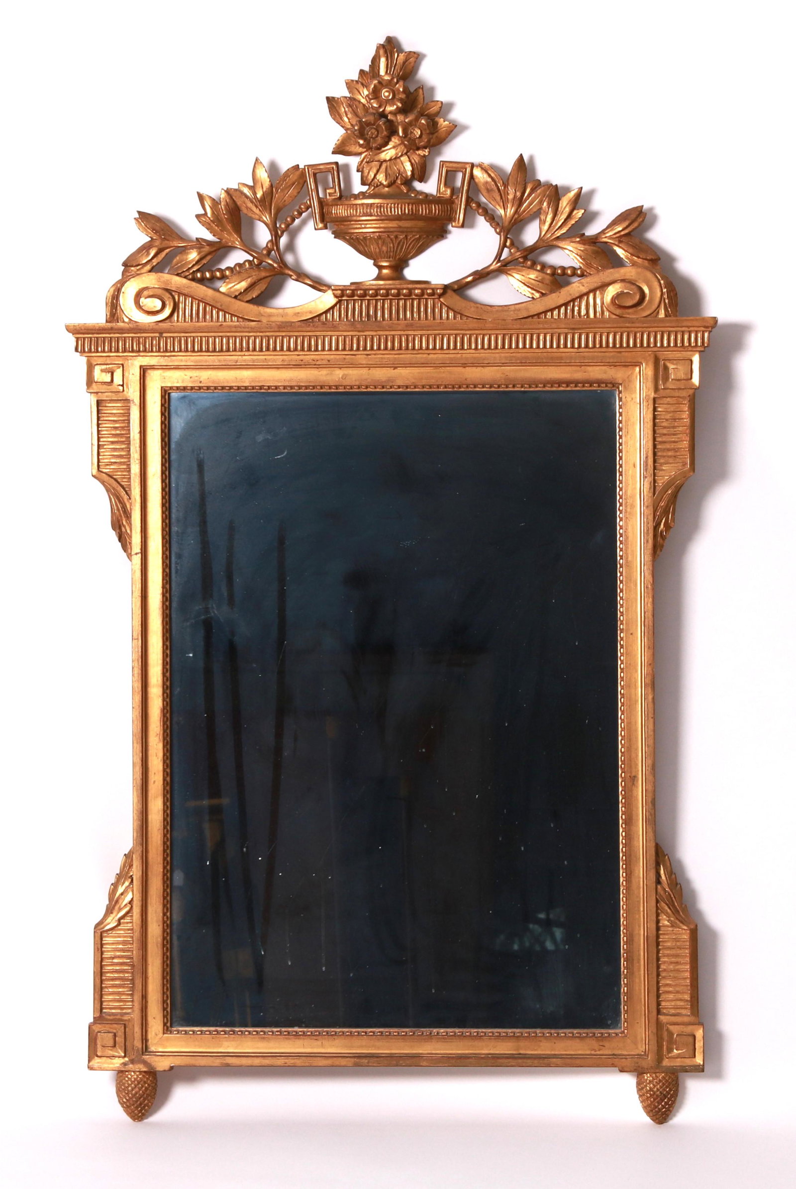 A Carved Giltwood Mirror: A 20th century neoclassical mirror with a crest that features a central urn with flowers. Dimensions: 34" x 58".