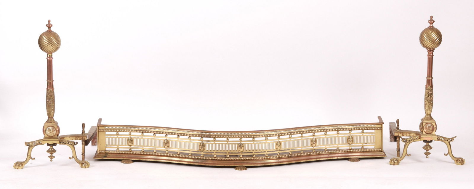 A Pair of Andirons and a Fender: All early 20th century, the andirons in brass and copper,each with ball and claw feet below acanthus knees below a shaft with central curved bracket below a spiral decorate ball finial. The fender fea