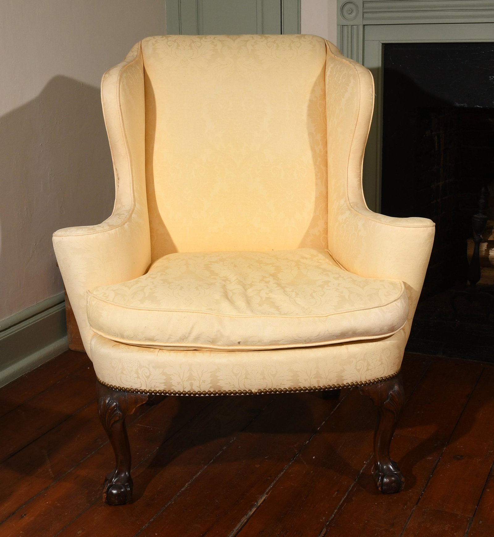 Chippendale Style Wingback Armchair: A Chippendale style carved mahogany wingback armchair, in the Philadelphia taste, 20th century, fully upholstered in a yellow Damask fabric. Dimensions:Height 42in; width 36 1/2in; depth 32in; seat he
