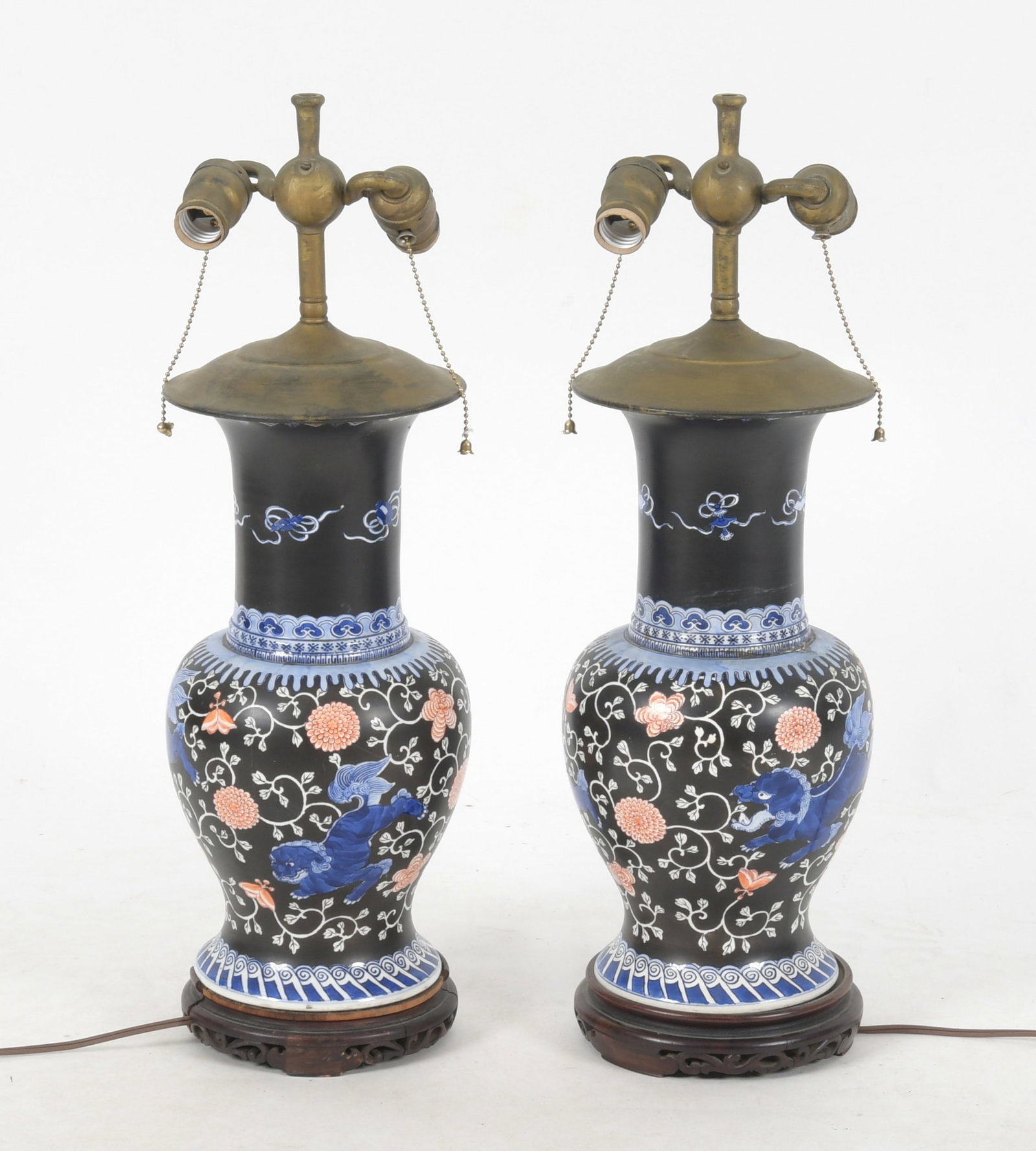 A Pair of Chinese Porcelain Lamps: A pair of early 20th century porcelain vases with a black ground and blue and red decoration that depicts flowers, auspicious symbols and foo dogs, mounted as lamps during the first half of the 20th c