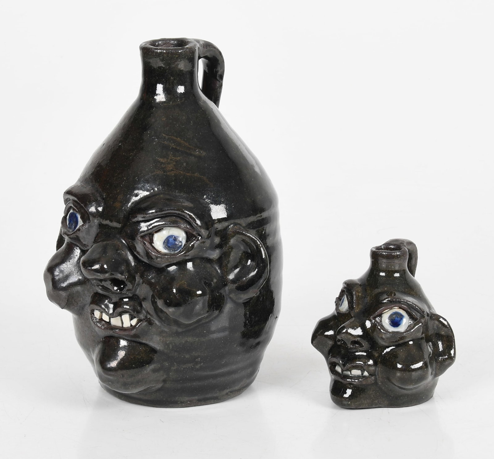 Two Grace Nell Hewell (Georgia, 1933-2016) Glazed Stoneware Face Jugs: Two Grace Nell Hewell (Georgia, 1933-2016) Glazed Stoneware Face Jugs Each with a strap handle, blue eyes, and China plate shard teeth. Each are signed and dated to the underside 'Grace Nell Hewel