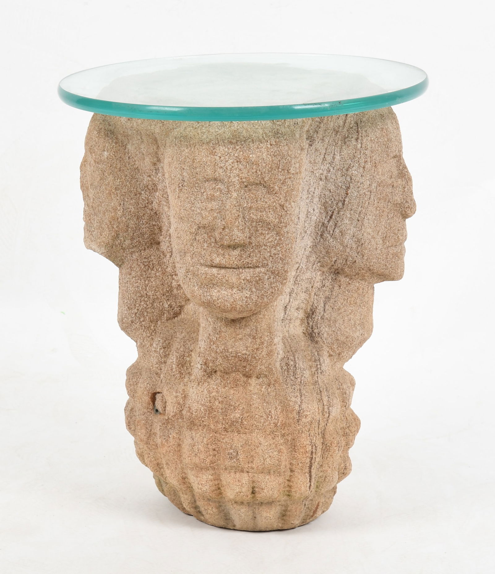 A Figural Carved Stone Side Table: A Figural Carved Stone Side Table Contemporary, with a glass top and carved with four heads facing outwards above a hobnail patterned foot. Dimensions: 13 1/2in in diameter, the
