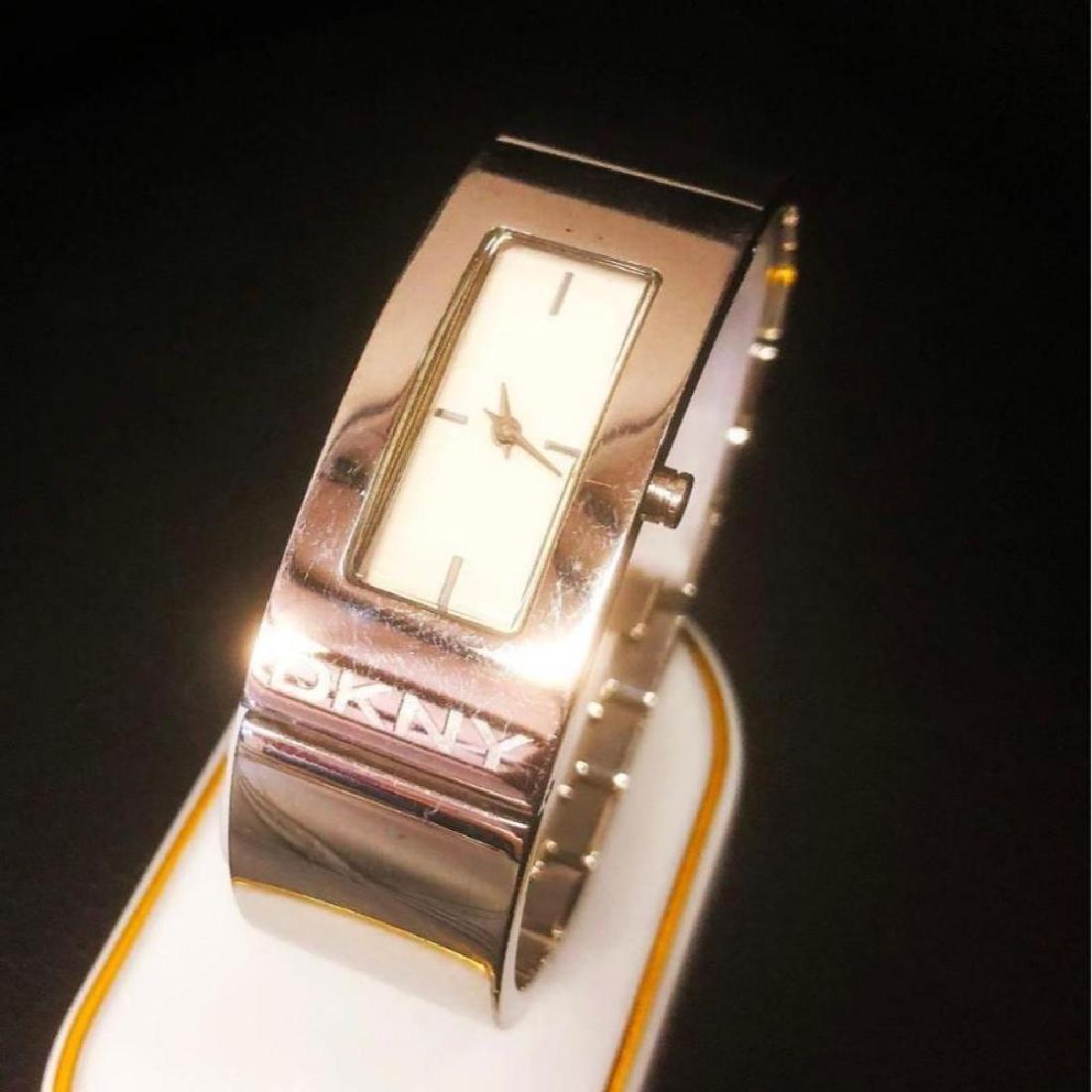 Ladies DKNY Watch: This attractive ladies DKNY watch is made from high polished stainless steel. It has an elegant rectangular case, with a simple etched DKNY logo on the bottom edge, matched with a half bangle style me