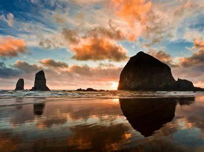 Haystack Rock at Sunset’s Glow: Haystack Rock at Sunset’s Glow  As the sun dips below the horizon, Haystack Rock stands tall against a sky painted in soft oranges and pinks. Fluffy clouds drift above, catching the last light of da
