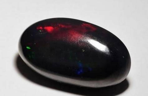 Cosmic Fire Black Opal Oval Cabochon: Cosmic Fire Black Opal Oval Cabochon  A gemstone of celestial wonder, this Black Opal features a smooth oval cabochon cut that reveals a breathtaking play of color. Against its deep black base, flashe