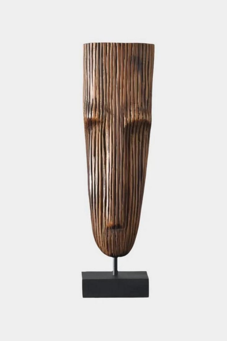 Hand-Carved Tribal Wooden Mask on Stand: Hand-Carved Tribal Wooden Mask on Stand This striking hand-carved wooden mask features elongated facial elements and deep vertical grooves that create a bold, textural design. Mounted on a sleek black
