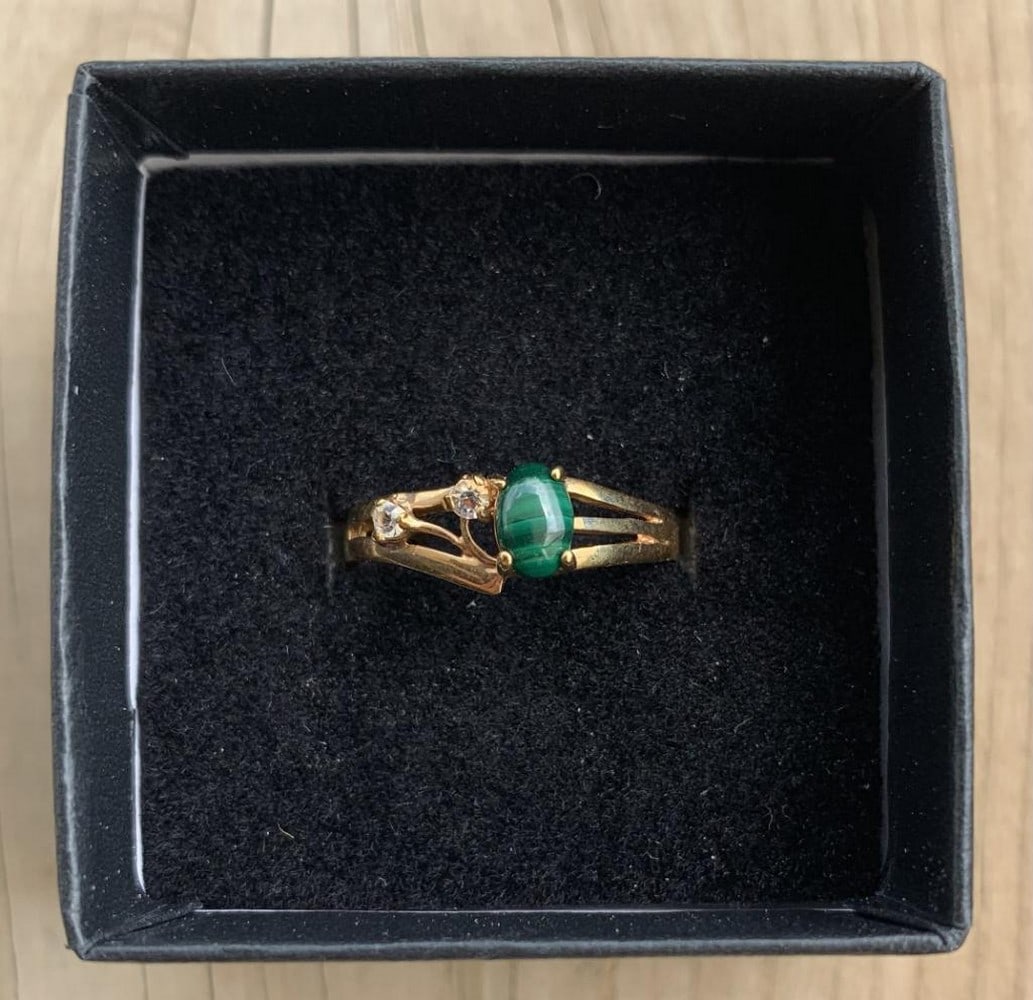 Banded Malachite Oval Ring: Banded Malachite Oval Ring This striking ring features a rich green malachite stone set in a warm 18kt gold electroplated band. Known for its natural banded patterns, the malachite adds a bold, earth