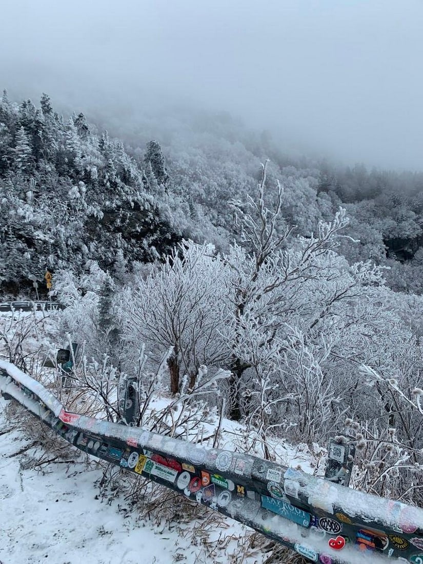 Misty Winter Road: Misty Winter Road The photograph captures a snow-covered landscape from the roadside, where icy trees and rolling hills disappear into a foggy, cloud-filled sky. In the forefront, a guardrail decorat