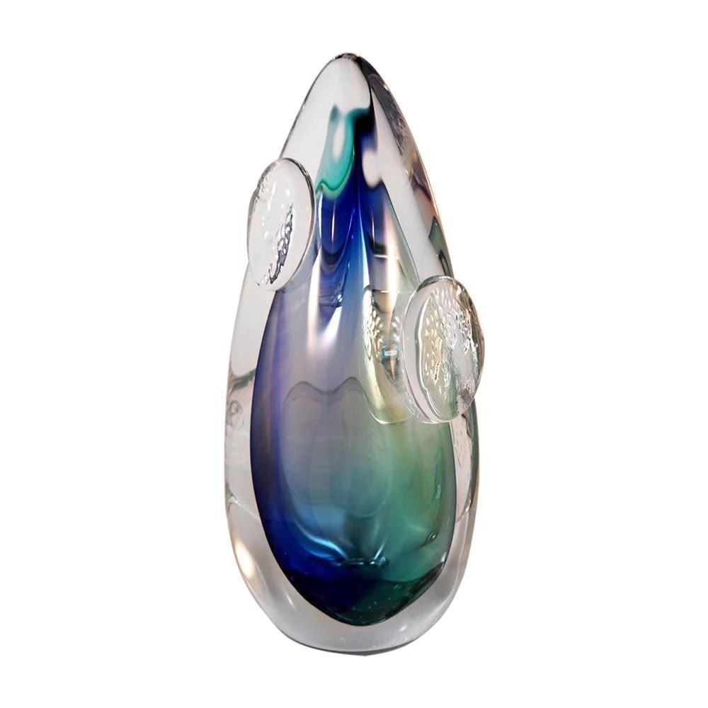 ‘Emblem’ Home Ornament by Remigijus Kriukas: ‘Emblem’ Home Ornament by Remigijus Kriukas Created by Lithuanian glass artist Remigijus Kriukas, the *Emblem* ornament stands tall in crystal clarity, infused with rich sapphire and azure