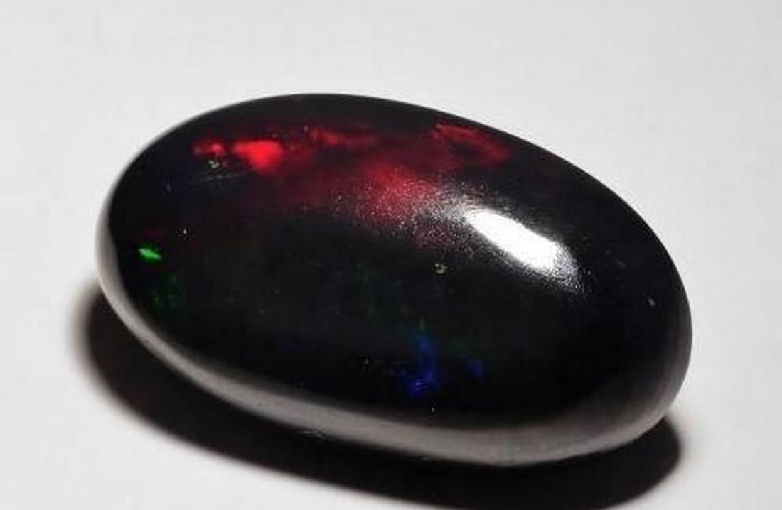 Cosmic Fire Black Opal Oval Cabochon: Cosmic Fire Black Opal Oval Cabochon A gemstone of celestial wonder, this Black Opal features a smooth oval cabochon cut that reveals a breathtaking play of color. Against its deep black base,